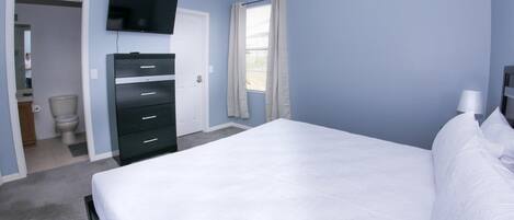 A bedroom with a bed, a dresser, a television, and a window with curtains.
