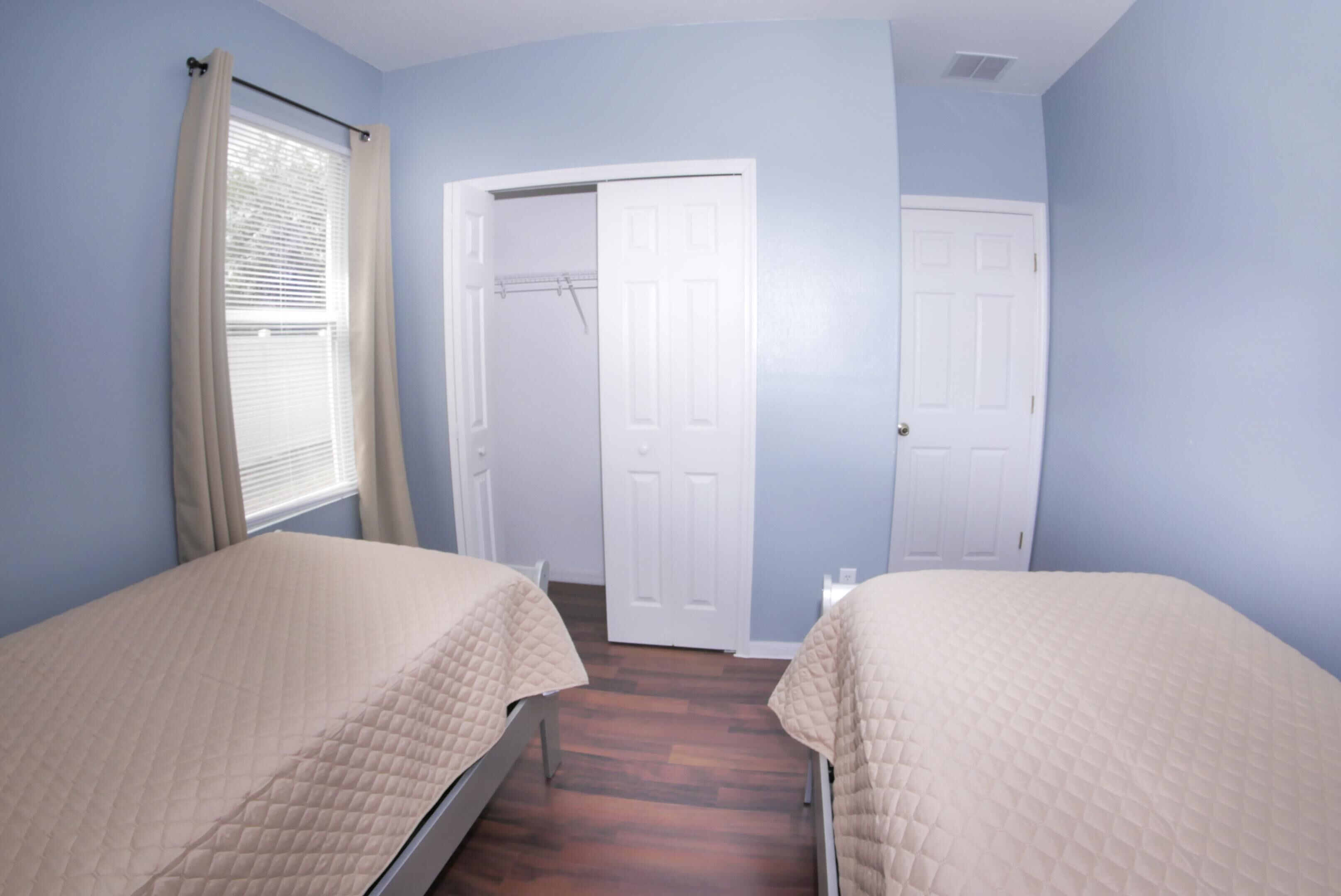 A bedroom with two beds, a window with curtains, and a door leading to another room.