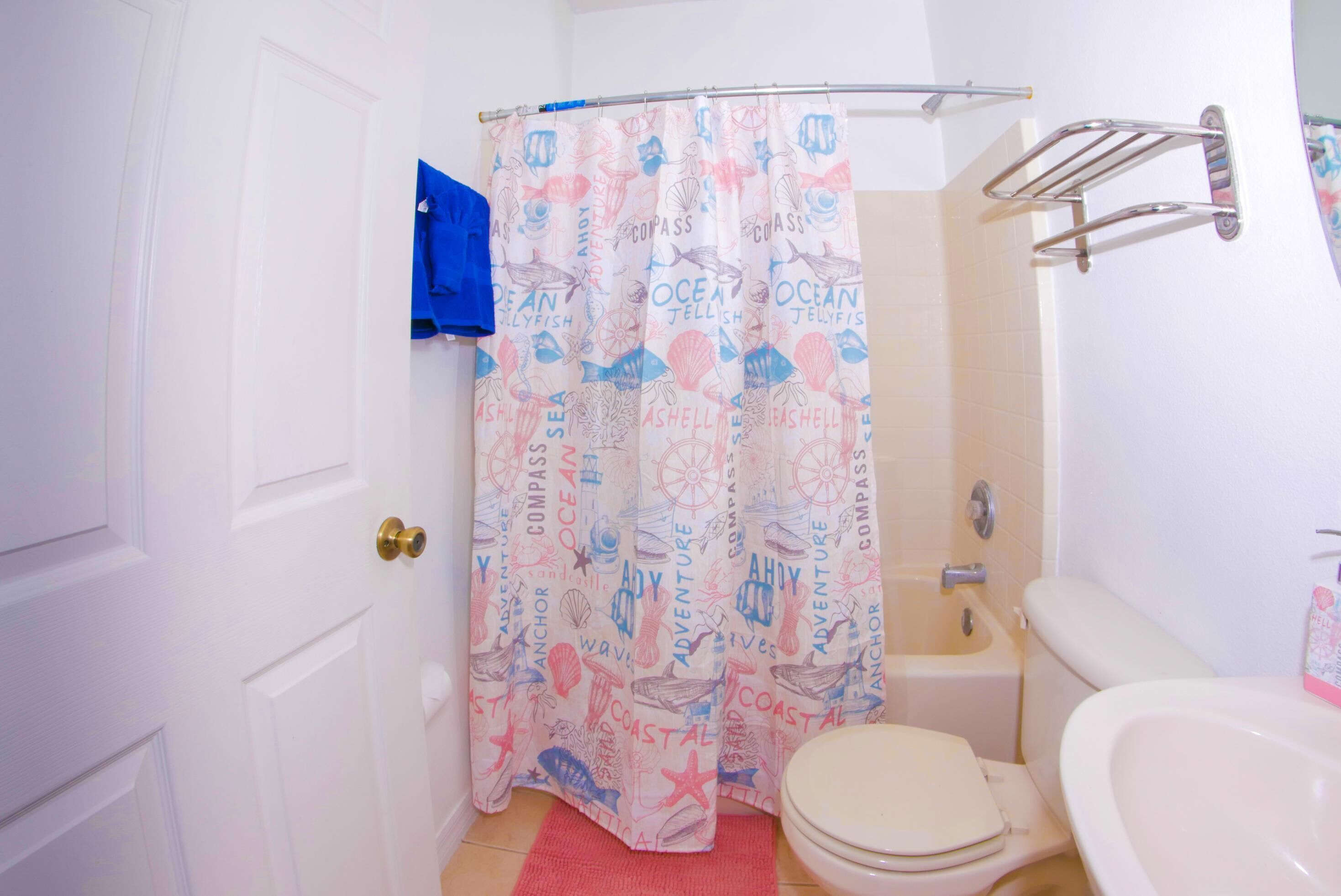 A bathroom with a white door, a shower curtain with ocean-themed prints, a bathtub, and a toilet.
