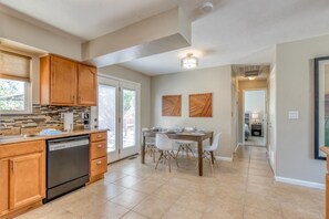 A modern kitchen with wooden cabinets, a dishwasher, and a dining area with a table and chairs. - Topo House II: Fenced Yard & Fire Pit Oasis (Fruita)