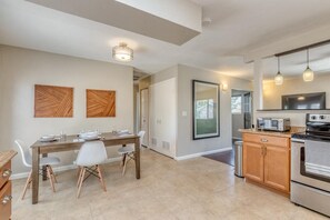 A modern kitchen with a dining area, featuring a wooden table, white chairs, a built-in oven, and a large window. - Topo House II: Fenced Yard & Fire Pit Oasis (Fruita)