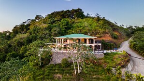 Une maison à deux étages, dotée d’un toit végétalisé, entourée d’une végétation luxuriante et bordée d’une route sinueuse.