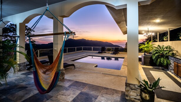 Un espace piscine sur le toit, avec un hamac, des sièges d’extérieur et une vue sur le coucher de soleil derrière les montagnes.