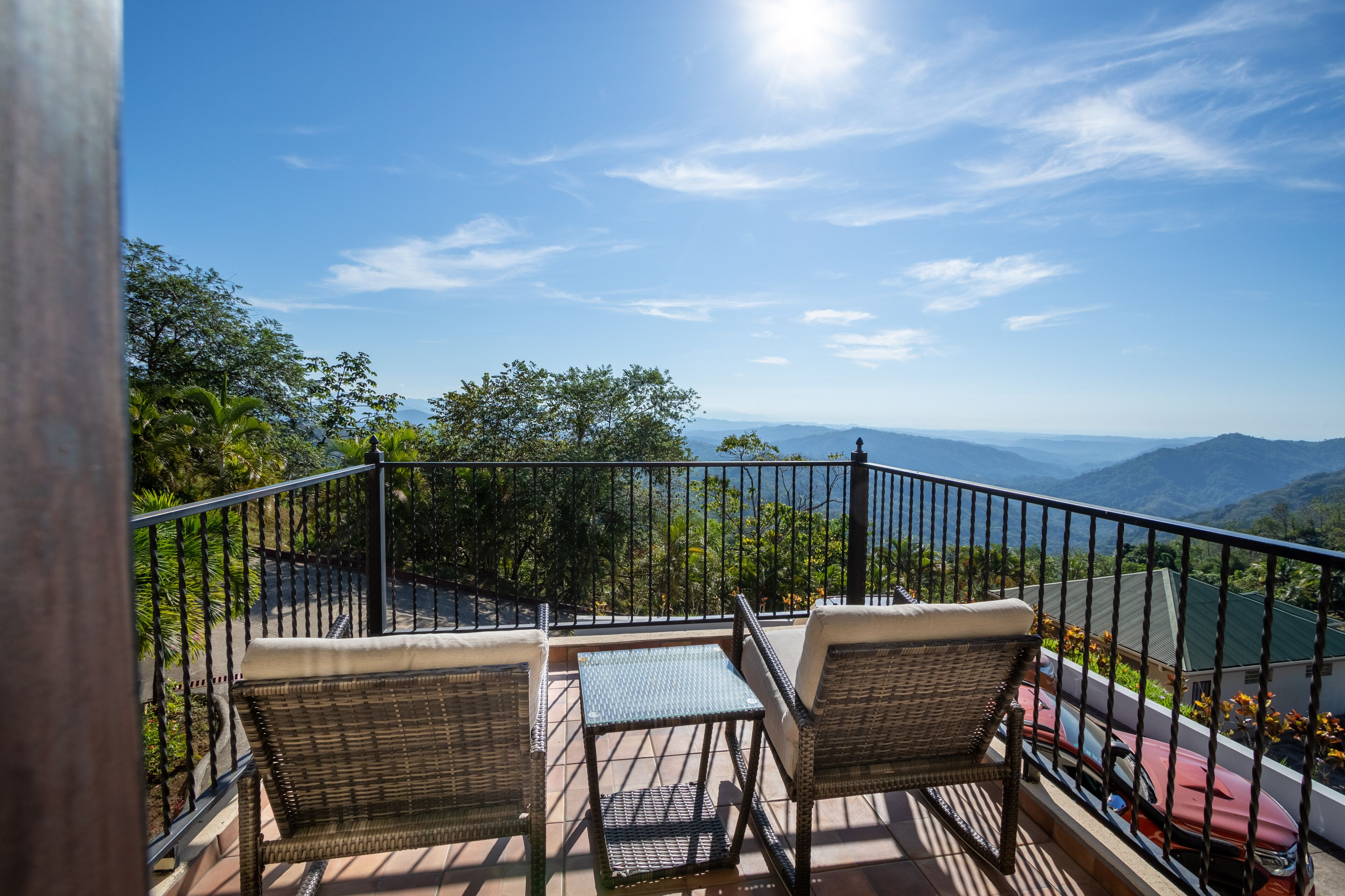 Un balcón con mobiliario de mimbre, una mesa y vistas a las montañas y un cuerpo de agua.