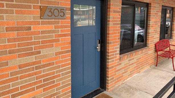 Un edificio de ladrillo con una puerta azul, un cartel de número y un banco rojo en el exterior.