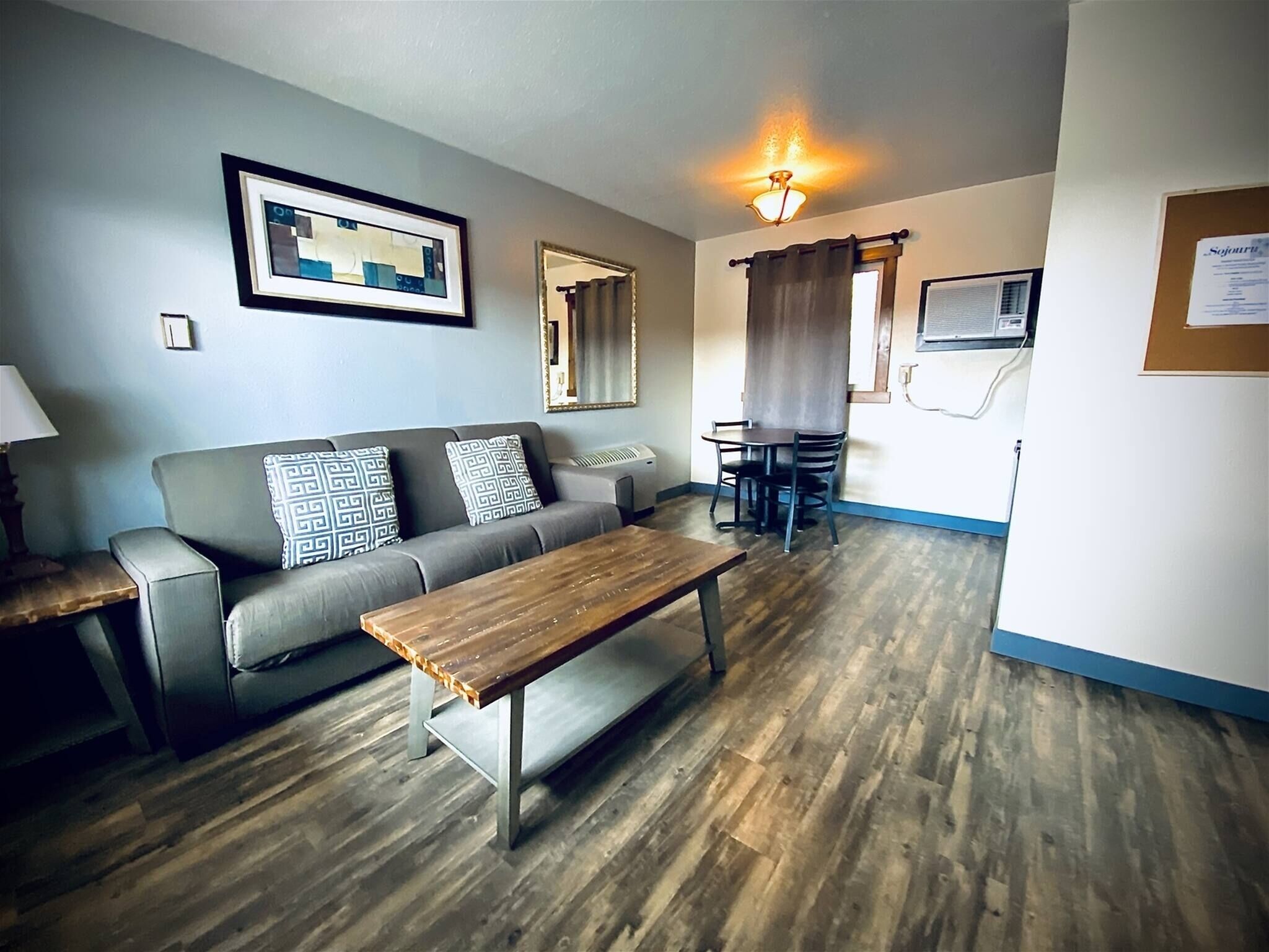A living room with a sofa, a wooden coffee table, a dining table with chairs, a mirror, and a ceiling light fixture.