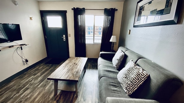Una sala de estar con una mesa de centro de madera, un sofá con cojines estampados, un televisor montado en la pared y una puerta que da a otra habitación.