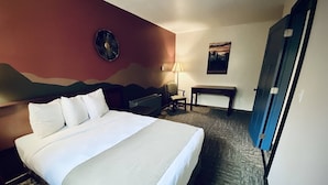 Habitación de hotel con una cama grande, un escritorio, una silla, una lámpara y una puerta.