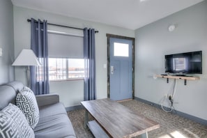 A room with a sofa, a wooden table, a television mounted on a shelf, a door, and a window with curtains.