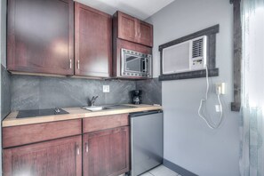 A compact kitchen with dark wooden cabinets, a stainless steel sink, a microwave, and a built-in air conditioner.