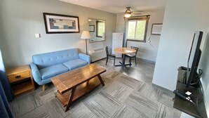 Een woonkamer met een blauwe bank, een houten salontafel en een eethoek met een tafel en stoelen.