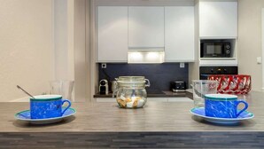 A modern kitchen with white cabinets, a microwave, and a glass jar on the counter. - Colombe - Furnished apartment - Downtown Lyon (Lyon)
