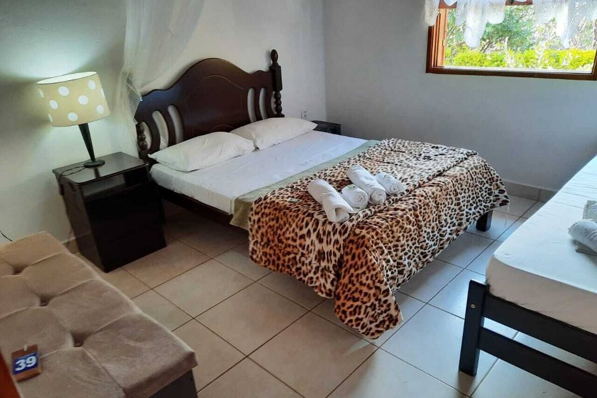 Un dormitorio con cama, mesita de noche, silla y ventana con vistas a zonas verdes.