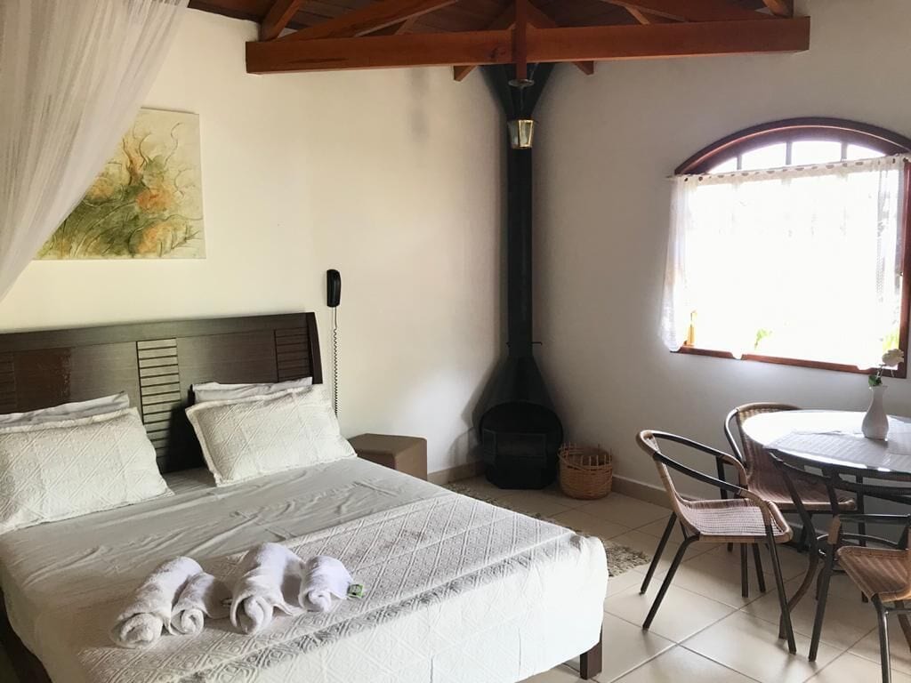 Quarto com cama, cabeceira, janela, mesa e cadeiras, e lareira.