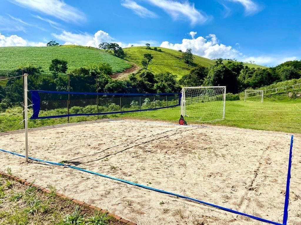 Un terrain de volleyball de sable avec un filet, entouré d’une clôture et d’arbres.