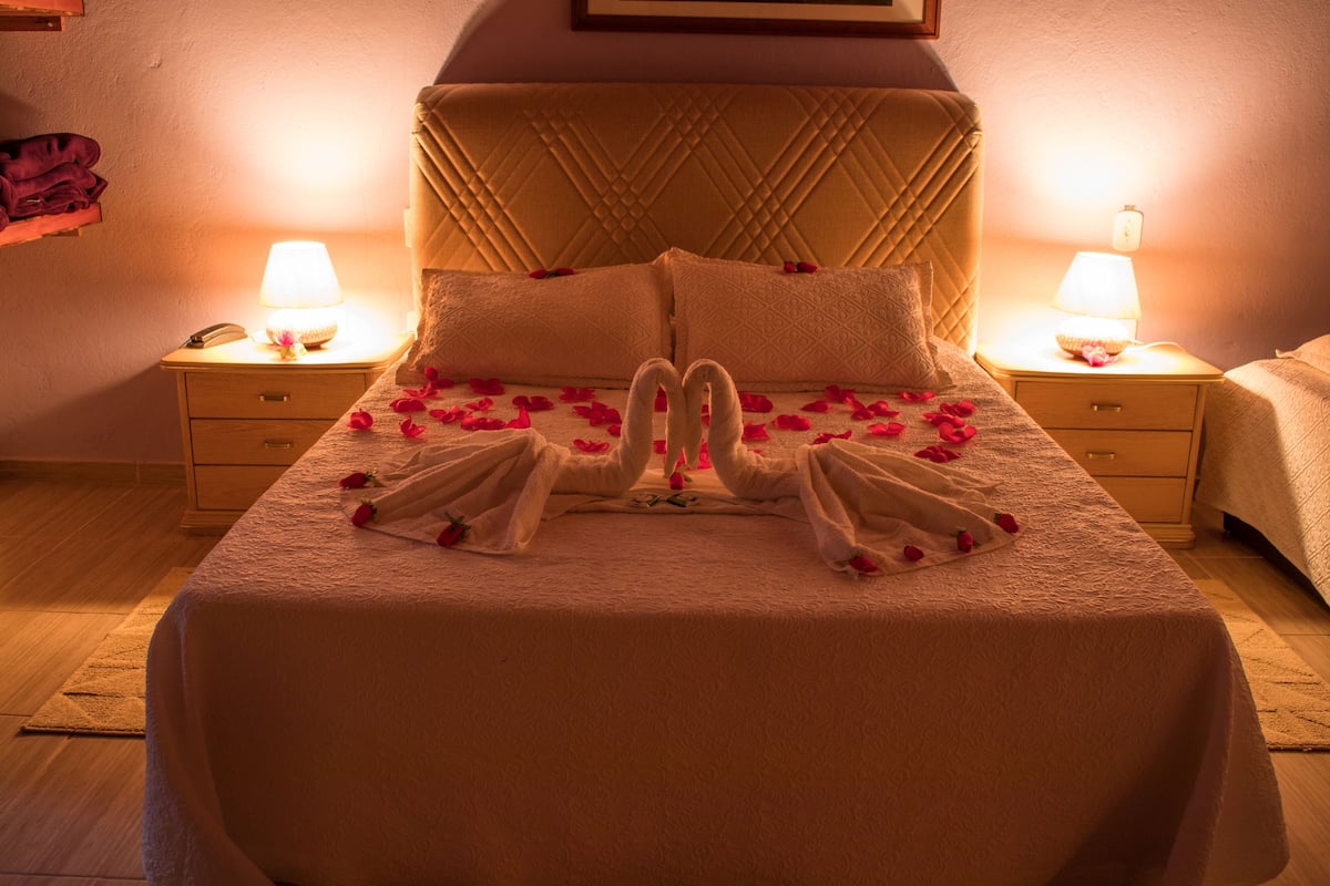 Una habitación de hotel con una cama, dos mesitas de noche y un tocador.