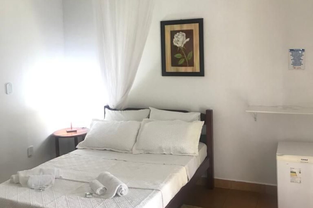 Une chambre d’hôtel avec un lit, un ventilateur de plafond, un tableau encadré au mur, une petite table et un réfrigérateur.