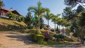 A residential property with a paved driveway, palm trees, and a red building with a sloped roof. - Pousada Sonho Meu (Itanhandu)