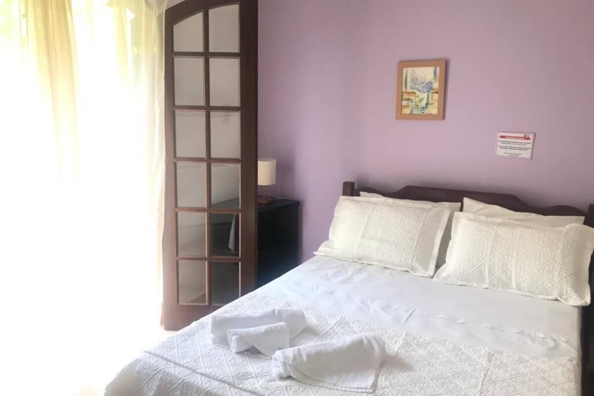 Una habitación con cama, mesita de noche, espejo y un cuadro colgado en la pared.
