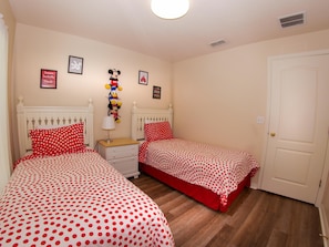 A bedroom with two beds, each with red polka dot bedding, a nightstand with a lamp, and wall decorations including framed pictures and a Mickey Mouse figure.