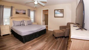 Un dormitorio con cama, televisor, ventilador de techo y piso de madera.