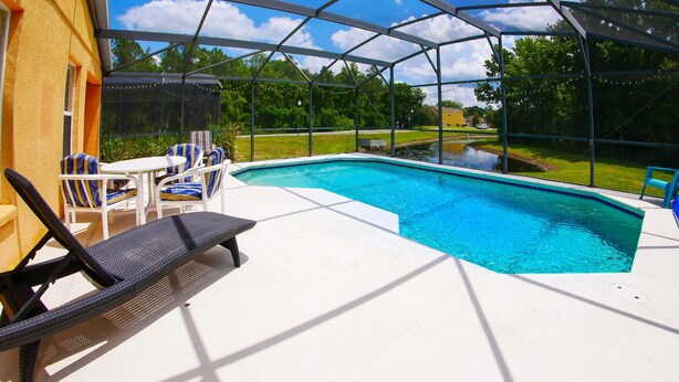Una piscina exterior techada con sillas de descanso y una mesa, rodeada de un paisaje verde.