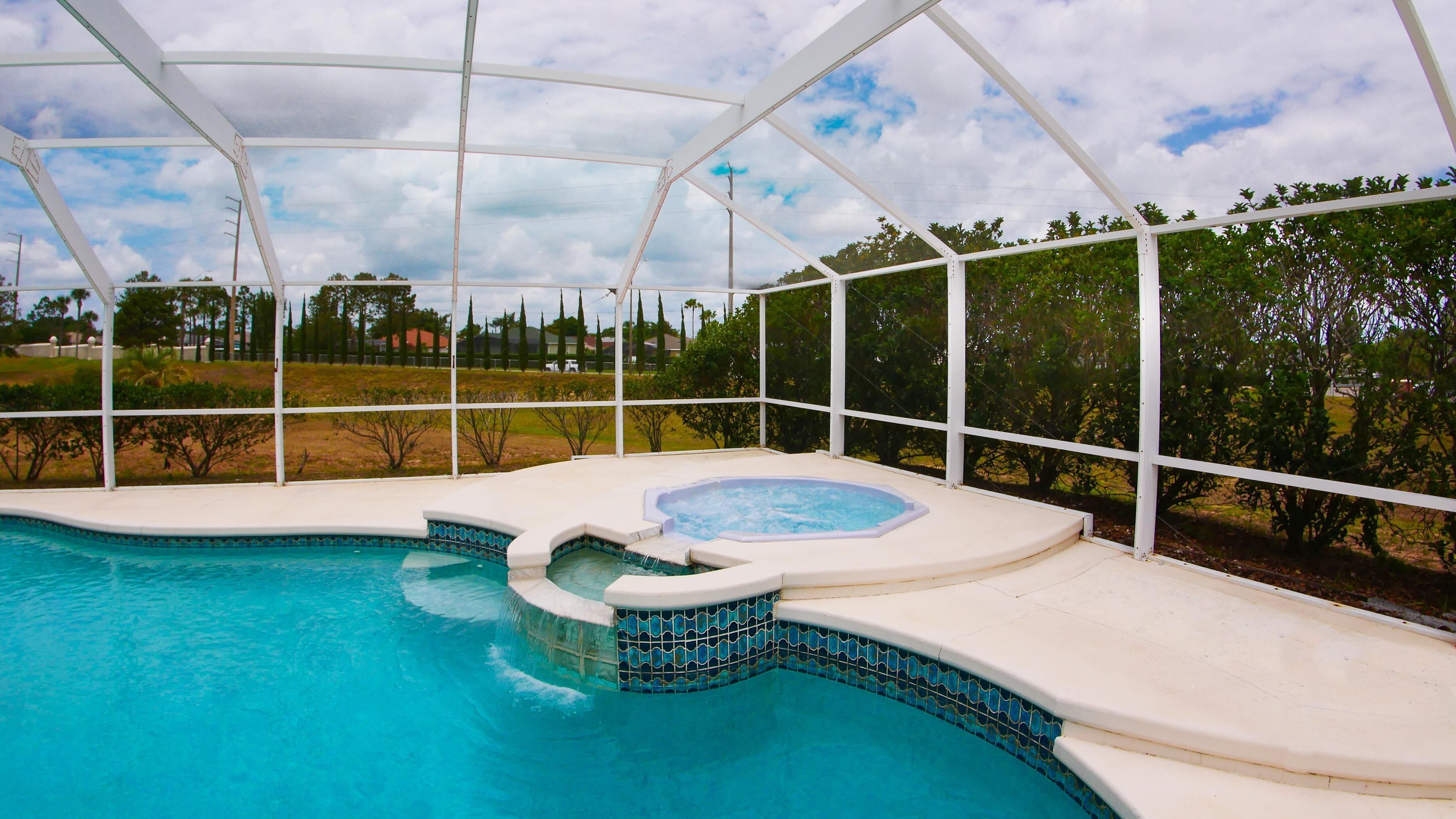 Una piscina interior con un jacuzzi, rodeada por una zona techada con vista a un barrio residencial.