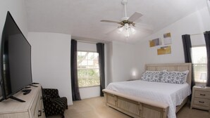 Een slaapkamer met een bed, een televisie, een bureau en een plafondventilator.