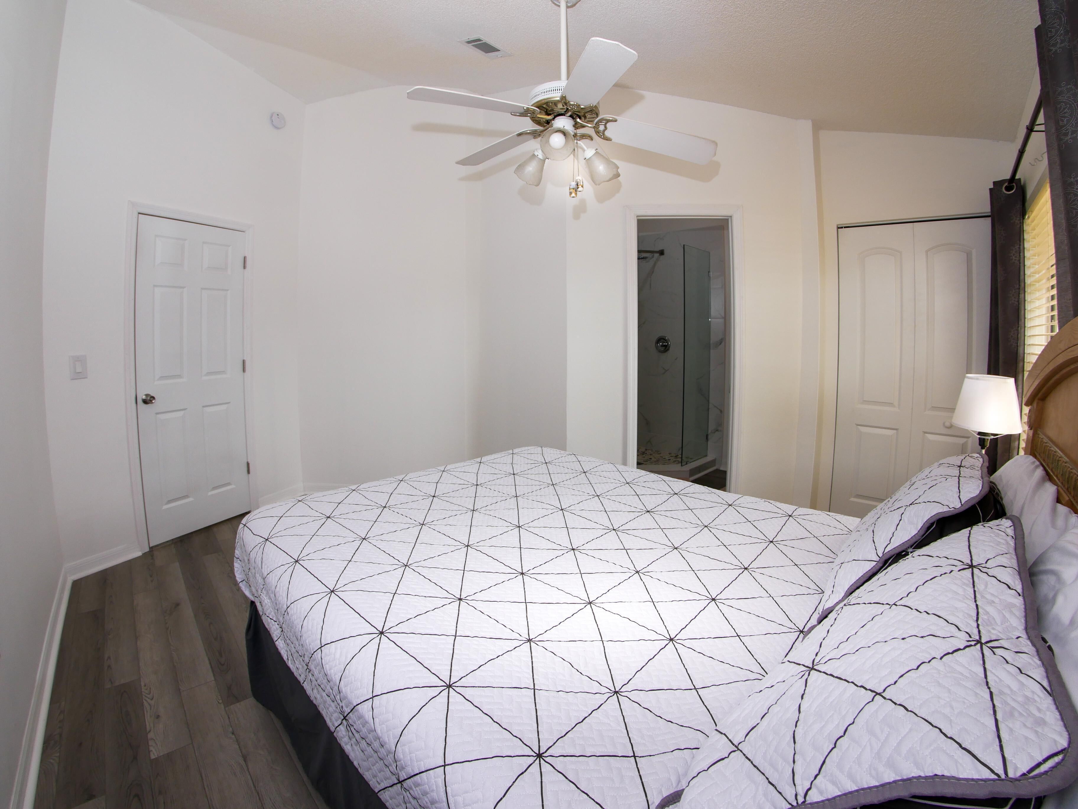 A bedroom with a bed, a ceiling fan, a door, and a shower area.