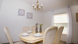Een eetkamer met een ronde tafel, vier stoelen, een kroonluchter en twee decoratieve wandborden.