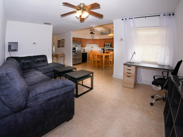 A living room with a sofa, a small table, a ceiling fan, and a view into the kitchen. - Large Pool With Jacuzzi, Near the Disney Attractions!! (Davenport)