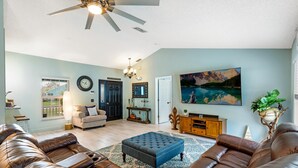 A spacious living room with a large brown leather sofa, a blue ottoman, and a ceiling fan. - Private Pool House, Near all Famous Attractions!!! (Kissimmee)
