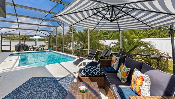 A covered outdoor pool area with lounge chairs, a sofa, and a table. - Private Pool House, Near all Famous Attractions!!! (Kissimmee)