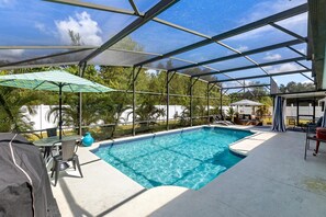 A covered outdoor swimming pool with a glass enclosure, surrounded by lounge chairs and umbrellas. - Private Pool House, Near all Famous Attractions!!! (Kissimmee)