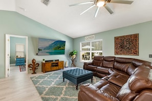 Uma sala de estar com um sofá de couro marrom, um banquinho azul, um armário de madeira e um quadro na parede.