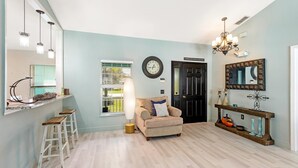 A living room with a sofa, a coffee table, and a chandelier. There is a door and a window with blinds. - Private Pool House, Near all Famous Attractions!!! (Kissimmee)