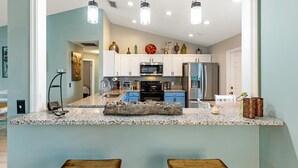 A modern kitchen with granite countertops, white cabinets, and stainless steel appliances. There are two wooden bar stools in front of the kitchen island. - Private Pool House, Near all Famous Attractions!!! (Kissimmee)