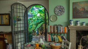 A dining area with a table set for breakfast, surrounded by bookshelves, a fireplace, and a view through a window with a tropical backdrop. - borgo antico resort diffuso (Bassano in Teverina)