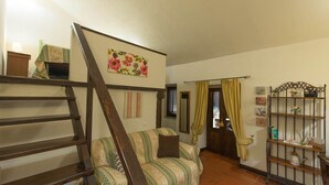 A cozy living room with a wooden staircase, a striped sofa, a floral painting, and a metal shelf with decorative items. - borgo antico resort diffuso (Bassano in Teverina)