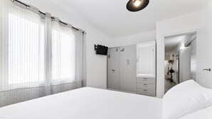 Un dormitori amb un llit gran, un armari amb molts calaixos, un mirall i cortines transparents.