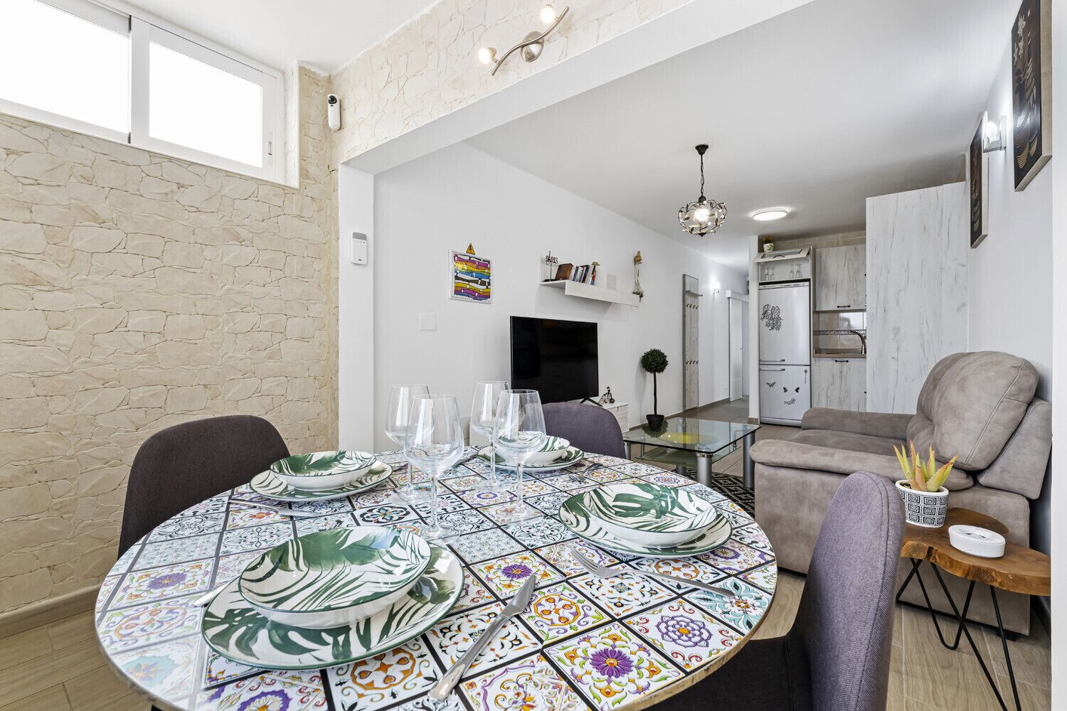 A dining area with a round table set for four, a sofa, and a kitchen in the background.