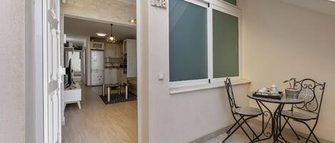 En kompakt lägenhet med ett litet kök, en matplats med bord och stolar samt ett stort fönster med utsikt.
