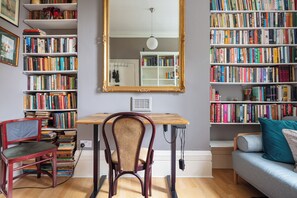 A study room with a wooden desk, a red chair, a bookshelf, a large mirror, and a grey sofa. - Ultra Central London | Leafy Street | Garden | King Bed | King's Cross (London)