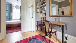 A bedroom with a bed, a desk, a chair, a bookshelf, and a large mirror.