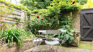 A garden with a metal chair and table, a stone wall, and a wooden gate.
