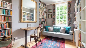 A cozy reading nook with a sofa, a chair, a desk, and a large bookshelf filled with books.