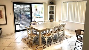 A dining area with a white table and chairs, a patterned rug, and a sliding glass door leading to an outdoor area. - Large Holiday Home with Heated Pool on demand near Lake & Beaches (Lake Munmorah)