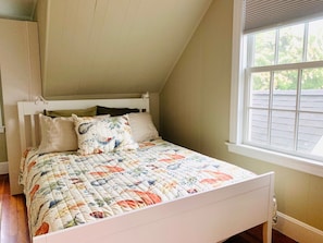 Ein Schlafzimmer mit einem weißen Bett, einem Fenster mit Jalousien und Blick ins Freie.