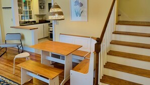 A cozy kitchen with a dining area, wooden staircase, and a hanging lamp.