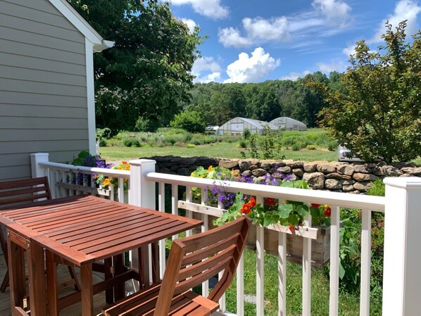 A wooden deck with a table and chairs, surrounded by a white railing with flower planters.